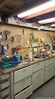 Wide view of pegboard and workbench holding an assortment of hand tools, hardware, and workshop supplies.