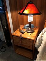 Lamp on wooden nightstand with belt, headphones, and blue telephone visible