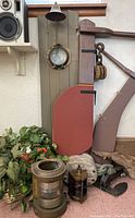 Full grouping of brass lamps, wooden rudders, bell, pulley, driftwood and anchor against wall