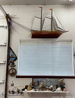 Overview of large wooden model sailing ship mounted above window with assorted nautical items and decor below on ledge and table.