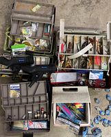 Overview photo showing multiple green and white tackle boxes filled with assorted fishing lures, lines, hooks, and other tackle, adjacent to two black West Marine fishing rod mounts.