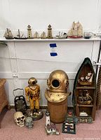 View of full lot showing scuba diver statue, brass helmet on wooden base, boat-shaped shelf with nautical decor, lantern and skulls on floor, and multiple miniature ships and lighthouses arranged on shelf above