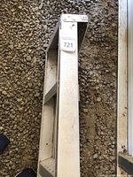 Top view of folded section of ladder showing flat metal frame and hinge points on gravel ground.