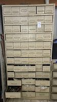 Front view of beige metal cabinet showing rows of small drawers filled with hardware