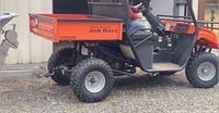 Side profile of orange UTV showing cargo bed, tubular frame and rear tire