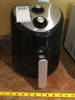 Full view of black Toastmaster air fryer with silver control knobs and handle, positioned on countertop with measuring tape indicating size.