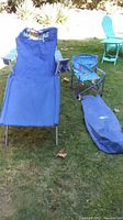 Blue folding camping chaise lounger with Marmaville logo, small child’s camping chair, and blue carrying bag on grass outdoors