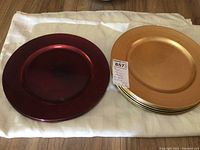 Photo showing a stack of 8 gold plastic plates and 4 red plastic plates side by side on a white cloth
