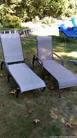 Two chaise loungers placed on grass outdoors, showing full length and design of each lounger with curved metal frames and grey mesh fabric seating.
