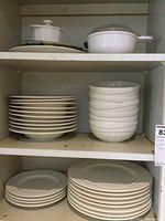 Top shelf view showing stacks of ceramic plates and bowls with white finish and wave design.