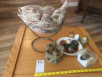 Wide shot showing all items: large ceramic fish on a metal stand, three-figure candle holder, multiple decorative eggs on a plate and surface.