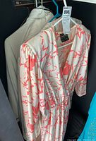 White dress with coral pink patterns, long sleeves, elastic waist, and wrap neckline on a hanger.