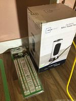 Photo showing boxed Mainstays Oscillating Mini Tower Fan alongside sealed BriteLED LED strips kit on floor.