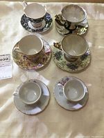 Six bone china tea cups with matching saucers, various floral patterns and gold trim.