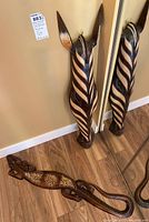 Horse head and lizard wood carvings on floor; horse head standing, lizard lying flat showing its decorative patterns.