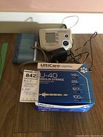 The box of UltiCare VetRx U-40 insulin syringes shown next to the LIFESOURCE blood pressure monitor, cuff, and power adapter on a wooden floor.