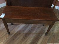 Wooden piano stool in brown finish, side view showing rectangular shape and straight legs