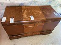 Front angle of the wood storage chest showing its rectangular shape, decorative veneer and surface wear.