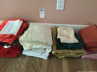 Multiple stacks of folded table linens and napkins in various colors arranged on a wooden surface.