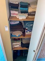 Image of folded assorted towels and linens stacked on shelves inside a closet.
