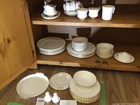 Full view of the fine bone china set including plates, cups, saucers, cream and sugar bowl, and salt and pepper shakers arranged in wooden cabinet and on floor.