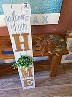 Photo showing full view of the wooden wall hanging sign with 'Welcome to Our Home' text and the ceramic sun decoration on a table.