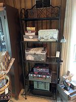 Full view of metal bakers rack with five shelves holding decorative boxes and clip-on light on right side.