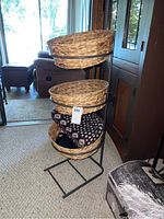 Front angled view of metal shelf with three woven baskets inside metal rings. Shelf stands on carpet in a living area.