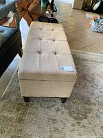 Full side view of the brown linen upholstered bench with tufted top and wooden legs.