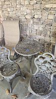 Side view of resin round table and two chairs with rose flower design against stone wall.