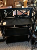 Front view of the black folding bookcase showing three shelves and decorative cross-bracing on sides.