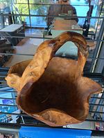 Handmade burl wood basket with natural wood grain and curved handle in front of a glass window.