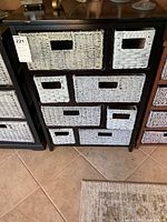 Front view of black wooden cabinet showing all seven gray woven baskets in various sizes arranged inside compartments.