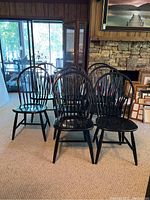 Group of black painted Windsor chairs arranged on carpet in front of stone fireplace