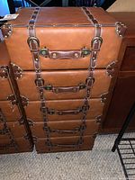 Front view showing five drawers with leather handles, faux leather covering, stitched straps, and metal buckle hardware.