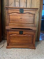 Pair of wood chests stacked, showing hinged lids and metal latches; top chest latch is lighter colored metal, bottom latch dark metal.