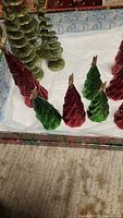 Glittery red and green cone-shaped Christmas tree figurines in different sizes displayed on white surface