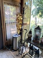 Full view of black metal coat rack with umbrella stand base and hanging shell wind chimes in an enclosed porch area.