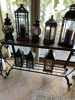 Photo showing all seven lanterns displayed on a wrought iron and wood table, highlighting their varying sizes, shapes, and finishes.