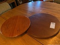 Two solid wood Lazy Susans shown side by side on a wooden table, one lighter and smaller, the other larger and darker.