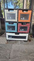 Front view of cabinet showing five wire baskets with wooden fronts labeled No. 1 to No. 5 in various colors including cream, orange, teal, and red.