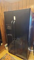 Front view of black Frigidaire side-by-side refrigerator with vertical handles and dispenser on left door.