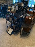 Photo showing black metal shelving unit with three curved tiers, lattice shelves and decorative scrollwork, alongside metal folding shelf.