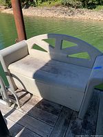 Side and front views of beige Rubbermaid plastic storage bench, weathered, bolted to dock near water.