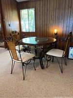 Full view of round dining table and three matching chairs in wood-paneled room.