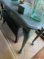 Close-up of the Cabrio leg and curved table edge with distressed greenish-gray paint.