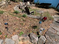 View showing red gazing ball on stand, ceramic turtles, metal whirligig, and shepherd's hooks with blue metal spinners in a garden setting with stone borders.