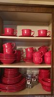 Top shelf with six red cups and matching saucers