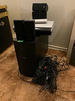 Photo showing the large Bose subwoofer, DVD player/control unit, remote on top, and bundled wires on the floor.