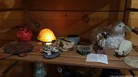 Wide shelf view of multiple animal figurines including a glass lamp shaped like a turtle with a yellow dome, red cardinal candle holder, several turtle figurines, and a textured white ceramic sheep with a green leaf and broken ear.
